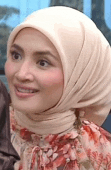 a woman wearing a hijab and a floral dress is smiling for the camera .