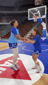 two female basketball players are shaking hands on a court with a sign that says ' basketball ' on it