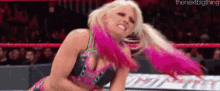 a woman in a pink and black wrestling outfit is standing in a ring .