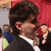 a man with a mullet hairstyle is wearing a tuxedo and white shirt