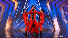 a group of men in red suits are dancing on a stage with a nbc logo in the corner