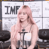 a woman with pink hair is sitting in front of a sign that says j.m.f group