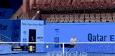 a man is playing tennis in front of a sign that says qatar