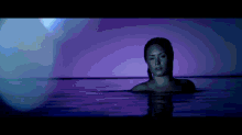 a woman is swimming in a pool with purple lights behind her .