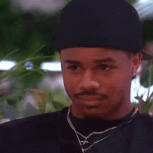 a man with a mustache is wearing a black hat and necklace