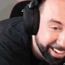 a man with a beard is wearing headphones and smiling while playing a video game .