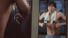 a shirtless man with a towel around his neck looks in the mirror
