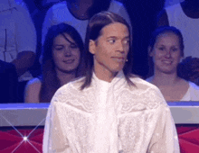 a man with long hair wearing a white shirt is sitting in a crowd .