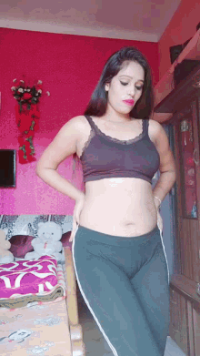 a woman in a bra and leggings is standing in a room with a pink wall .