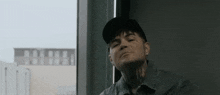 a man with a tattoo on his neck is sitting in front of a window wearing a hat .
