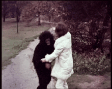 a woman in a white coat is holding a black chimpanzee