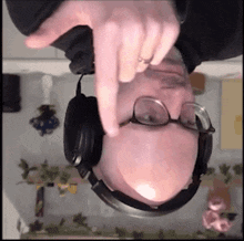 a man wearing headphones and glasses is upside down and pointing