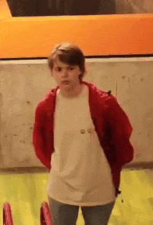 a person wearing a white shirt and a red jacket is standing in front of a yellow wall