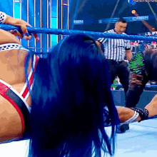 a woman with blue hair is in a wrestling ring with a referee and a sign that says win