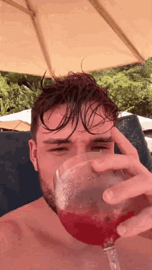 a man without a shirt is drinking a glass of red liquid