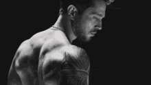 a black and white photo of a shirtless man with tattoos on his arms