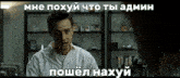 a man in a white shirt is sitting in front of a bookshelf in a room with a caption in russian