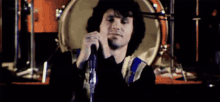 a man is singing into a microphone on a stage in front of a drum .