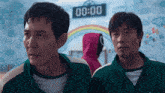 two men standing in front of a wall with a clock that says 00:00
