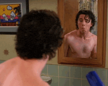 a man without a shirt is looking at himself in the mirror