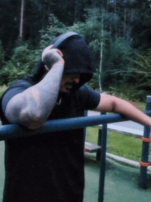 a man in a hooded shirt is leaning on a blue bar