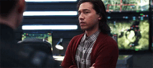 a man in a plaid shirt and a red cardigan stands in front of a monitor