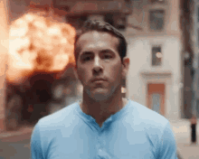 a man in a blue shirt is standing on a street in front of a building on fire .