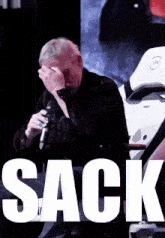 a man covering his face while holding a microphone with the word sack above him