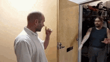 a man in a white shirt is knocking on a door while another man stands behind him