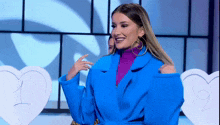a woman in a blue coat and purple turtleneck is standing in front of a heart .