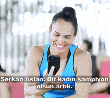a woman in a blue tank top is smiling and looking at her cell phone