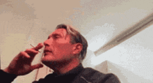a man is smoking a cigarette in a room while another man holds a cigarette to his nose .