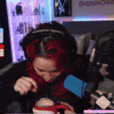 a woman with red hair is sitting in front of a microphone and drinking from a cup .