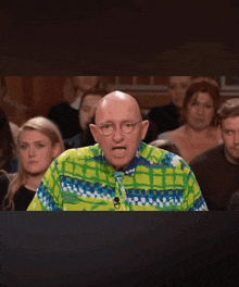a bald man wearing a colorful shirt and tie stands in front of a crowd of people