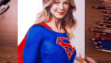 a drawing of a woman in a superman costume on a table with colored pencils .