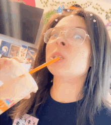 a woman wearing glasses is drinking from a plastic cup with a straw