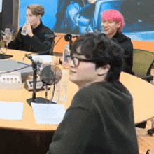 a group of people are sitting at a table with microphones . one of the people has pink hair .