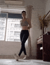 a woman in a sports bra and leggings is standing in front of a large window