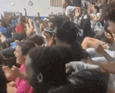 a crowd of people are sitting in a gym raising their hands in the air .