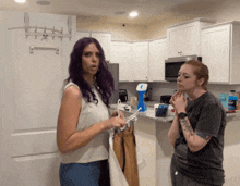 a woman with purple hair stands next to a woman with red hair in a kitchen
