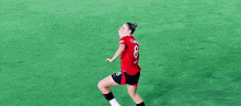 a female soccer player wearing a red jersey with the number 8 on it is kicking a soccer ball on a field .