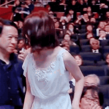 a woman in a white dress is standing in a crowd of people .