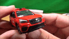 a red toy car is being held in a person 's hand .