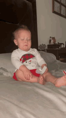 a baby is sitting on a bed with his eyes closed and a pacifier in his hand