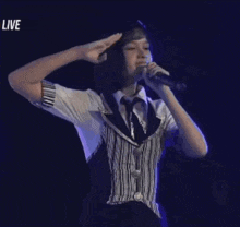 a woman in a striped vest and tie is saluting while dancing on a stage .