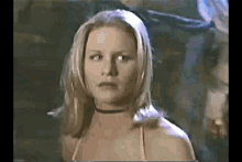 a woman with blonde hair and a choker around her neck is standing in a dark room .
