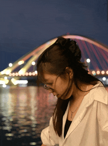 a woman wearing glasses and a necklace stands in front of a bridge