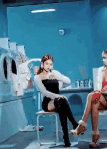 two women are sitting in a laundromat in front of a washing machine
