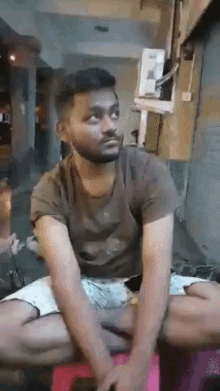 a man with a beard is sitting on a pink stool talking to another man .