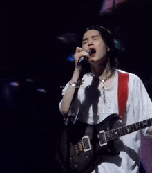 a man singing into a microphone while holding a guitar on stage